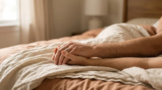 Silhouettes de deux mains entrelacees dans une lumiere douce et chaude, symbolisant la synchronisation intime d'un couple